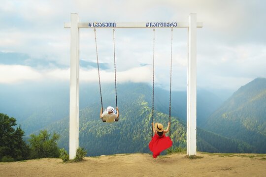 Young excited tourist couple together having fun on holidays swing on giant Mestia swings on Heshkili huts hilltop. Concept freedom, fun, travel. Mestia. Svaneti region.Georgia. Travel destination