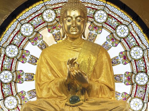 In the main chedi of Wat Phra That Sorn Kaew, the gilded Buddha statue shines out against a luminous glass mandala that fills the space with light and colour. The delicate patterns of the window and the gentle radiance of the robe combine to create an atmosphere of quiet contemplation. This photograph captures the unique harmony of spiritual symbolism, exquisite craftsmanship and meditative tranquillity: the main chedi (Phra That), Wat Phra That Sorn Kaew, Khao Kho Mountains, Phetchabun Province, Isan, Thailand