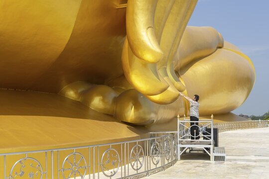 Largest Buddha statue in Thailand (Luang Pho Yai), woman 60-70 touches the fingertips of the statue because according to local belief this brings good luck and success, Wat Muang, Ang Thong, Amphoe Wiset Chai Chan province, Thailand