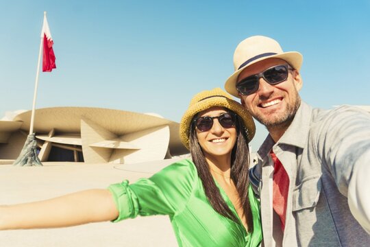 Doha, Qatar - 8th january, 2026: Happy young couple taking selfie in front of National museum of Qatar. Two tourists enjoy vacation in middle east - Holidays and traveling lifestyle concept