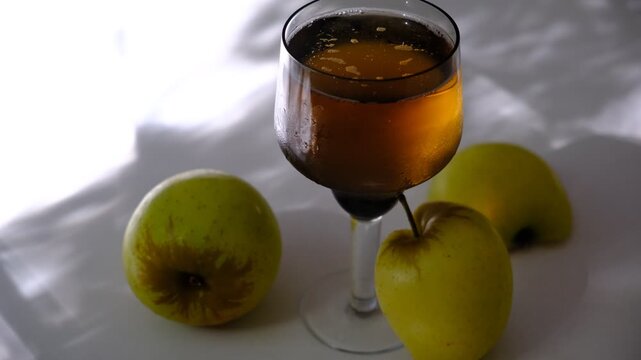 Glass of brut apple cider from Normandy. White table with casting shadows and sunlight. Ripe yellow fruits on the table. Atmospheric mood.	