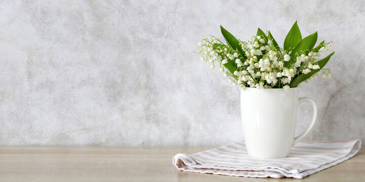 Bouquet of lily of the valley flowers in a white ceramic mug on a wooden table