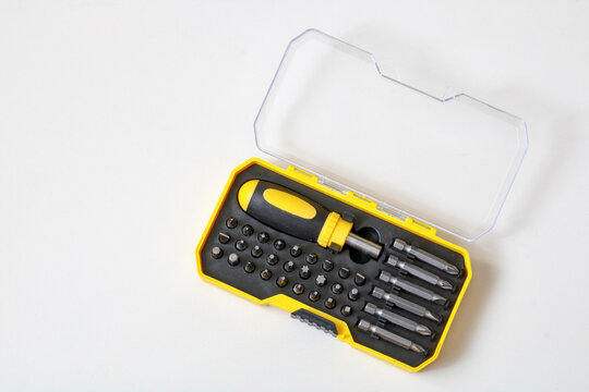 A open yellow plastic case containing a screwdriver handle and replaceable drill bits resting on a white background.
