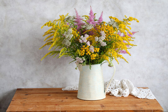 bouquet of flowers in a jug on the table: yarrow and astilbe, goldenrod and tansy. Summer still life, cottage decor and interior concept.