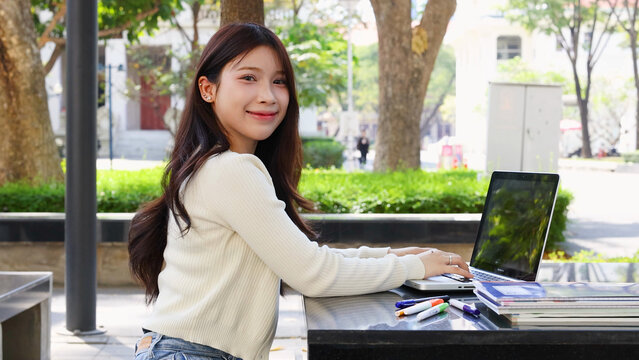 Smiling Young Thai Student Using Laptop at Outdoor University Campus Table
