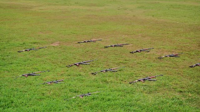 High-angle view of multiple assault rifles laid out in organized rows on green grass during military training drill practice.
