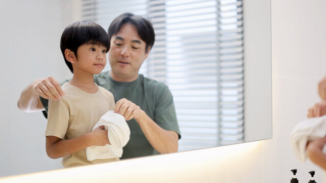 Asian Father Helping Young Son Dry Hands with Towel in Bathroom Mirror