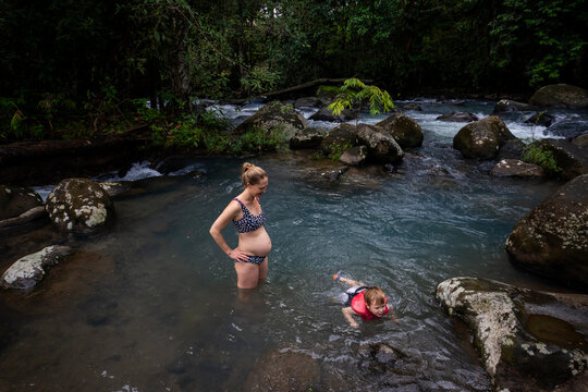 A young boy swims in a river alongside his mother.
