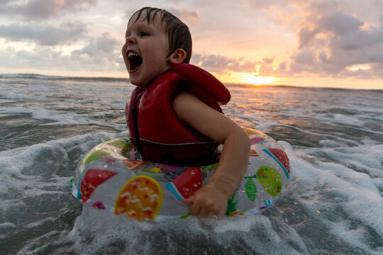 Young boy shouts with joy in ocean waves at sunset