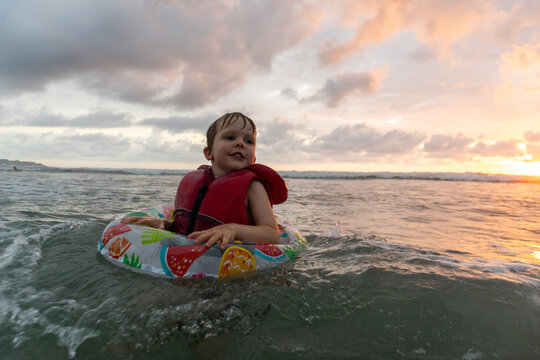 Happy little boy floating in the ocean at sunset