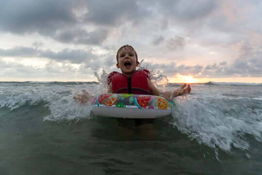 Joyful young boy splashes in ocean waves at sunset