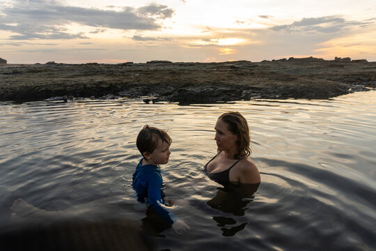 Mother and son talking in a rocky tide pool at sunset