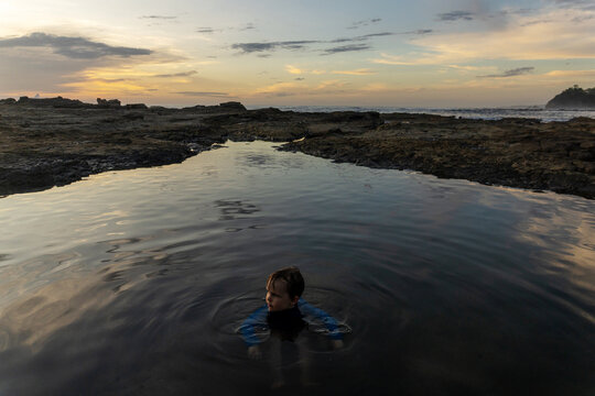 Young boy standing in a dark ocean tide pool