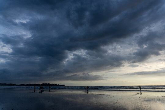 Surfers on the beach under a dark stormy sky