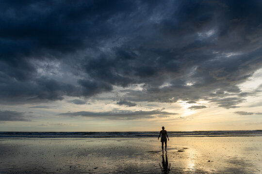 Man walks on reflective beach under stormy sky