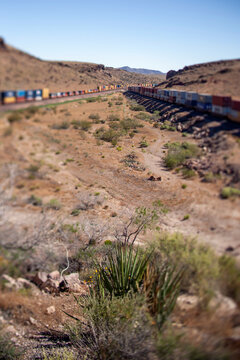 Long freight train snakes through desert with tilt shift vertical