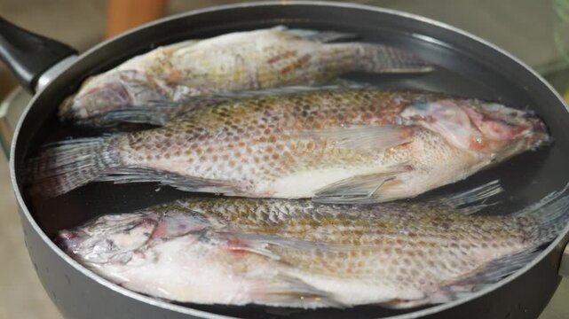 Black person squeezing lemon juice over raw whole tilapia fish