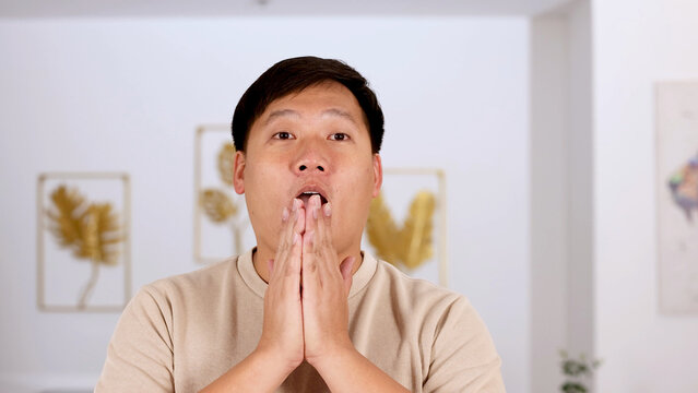 Surprised Asian Man Covering Mouth with Hands in Modern Living Room