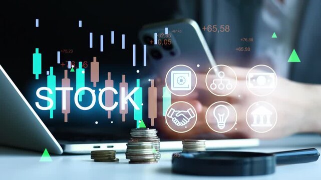 A person is looking at stock market data on a laptop while holding a smartphone. Financial charts and coins are visible on the desk. The scene takes place in an office.