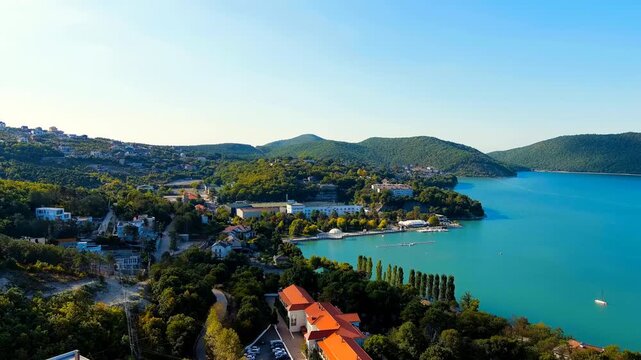 Abrau-Diurso, Krasnodar Krai, Russia. Lake Abrau. Embankment and village. Summer. The text on the embankment translates as the name of the village - Abrau-Diurso. Drone footage