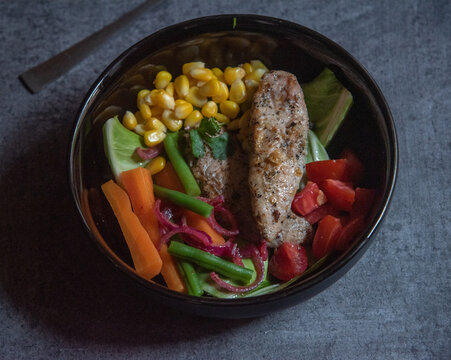 Grilled chicken breast with vegetables in a bowl on a black background. Close up, selective focus.