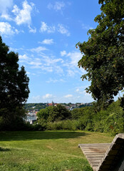 Obraz premium Scenic view of a green park in Flensburg, wooden bench overlooking a city skyline under a bright blue sky 