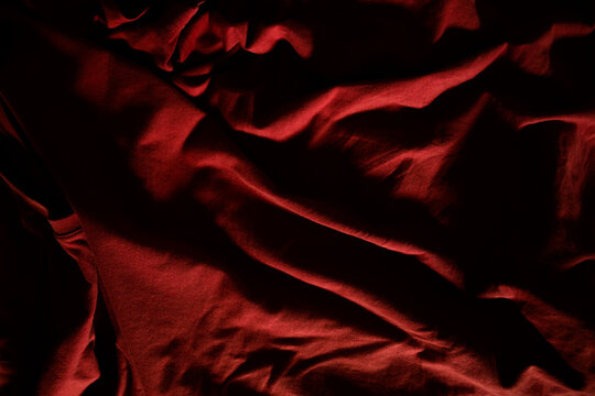 Abstract background texture of wrinkled crimson cloth with moody, high-contrast chiaroscuro light and shadow.