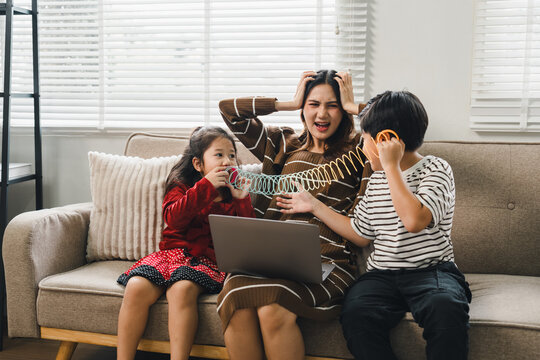 Stressed mother working on laptop while her children play noisily at home