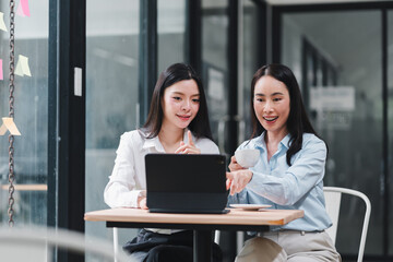 Obraz premium Two Asian businesswomen working together on a laptop computer in an office