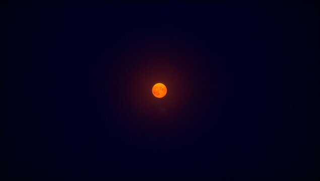 Bright orange full moon illuminated against a dark night sky, showcasing lunar surface details and a subtle halo effect surrounding the moon