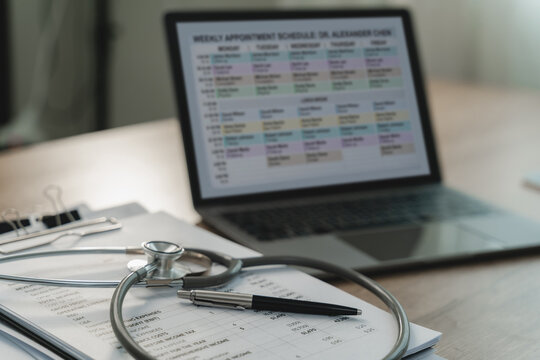 Stethoscope rests on clipboard beside laptop displaying weekly appointment schedule, highlighting medical records review, healthcare scheduling, documentation, administrative workflow on office desk.