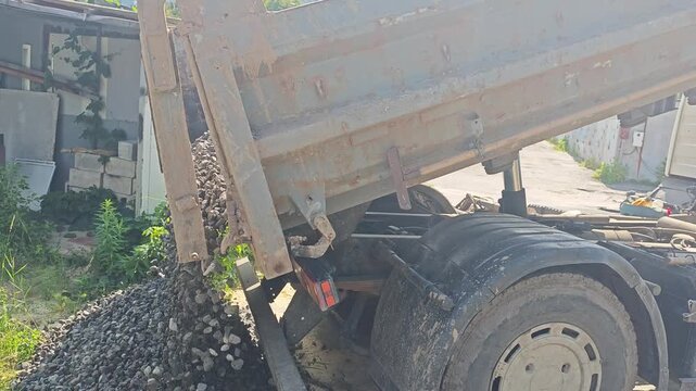 Close-up of a dirty dump truck unloading crushed stone or gravel at a construction site on a sunny day.