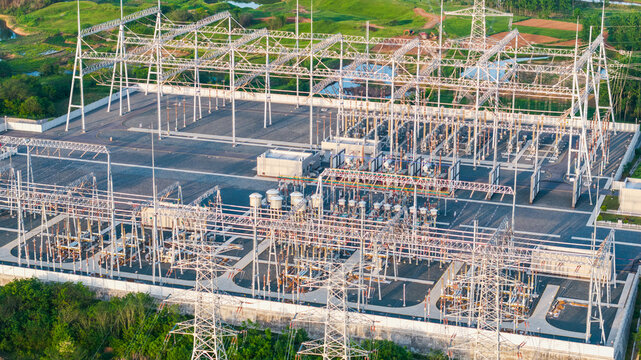 An aerial view of an outdoor high-voltage electrical substation with metal transmission towers and power equipment.