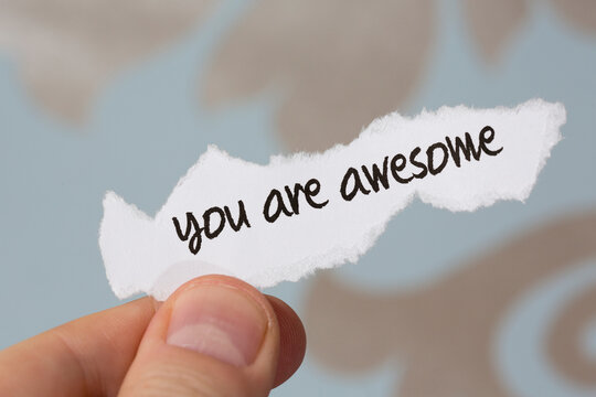 Romantic handwritten text on a paper note. A man is holding a piece of paper with text to her or him.. Text says you are awesome. 