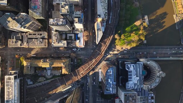 Top-down aerial drone video of Flinders Street and Spencer Street in Melbourne CBD, showing trains on elevated rail lines, vehicle traffic, city streets and morning light