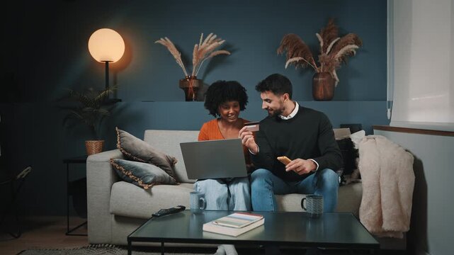 Young cheerful couple shopping at home with credit card and laptop, buying on digital retail shop doing online payment
