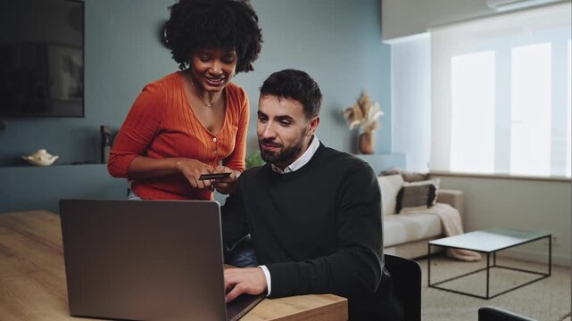 Young happy couple shopping at home with credit card and laptop, doing online payment