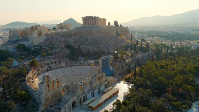 Athens, Greece. Acropolis of Athens and ancient Odeon of Herodes Atticus, aerial drone view ascending past stone amphitheater to Parthenon in warm morning summer light. Drone footage