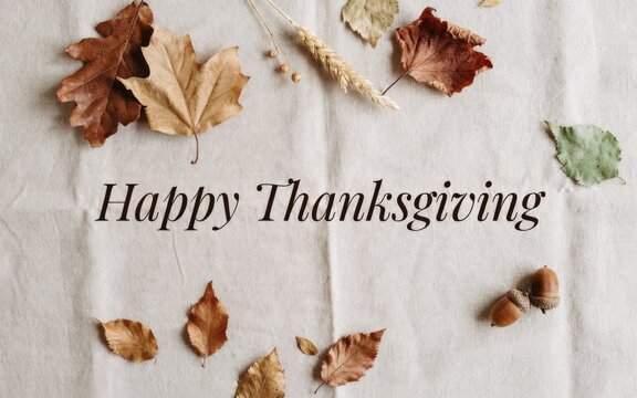 Happy thanksgiving day greeting card with dry autumn leaves arranged on a rustic white wooden background