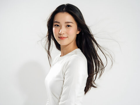 Young asian woman with long dark hair blowing in the wind, smiling, wearing a white shirt against a plain white studio background, side profile