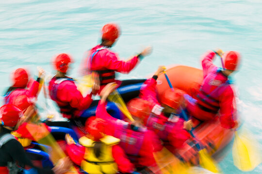 White water rafting adventure travel lifestyle featuring a team in red gear paddling a raft through cold, swirling blue river water in Julian Alps Natural Park, Resia, Friuli Venezia Giulia, Italy.