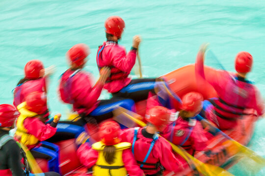 Rafting team in red gear paddling through turquoise river rapids during outdoor adventure, showcasing teamwork and active tourism in the Julian Alps Natural Park, Resia, Friuli Venezia Giulia, Italy.