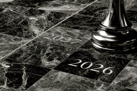 A chess piece stands on a marble board with the years 2026 and 2027 etched into the squares.