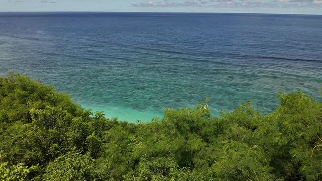 Turquoise reef waters framed by cliffside trees at Gunung Payung, Bali