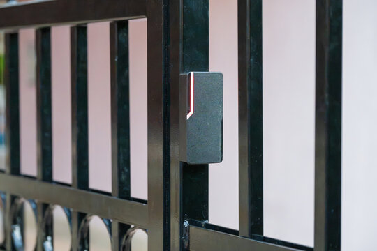 a modern electronic access control reader with a glowing LED indicator, mounted securely on a black metal gate to manage entry.