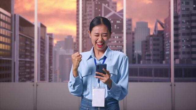 Asian Female With Her Smarphone at Office with Panoramic City Skyline at Sunset, She Raises Her Fist Up With Screaming Goal