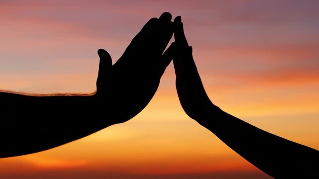 Two hands reaching for a high five against a sunset sky