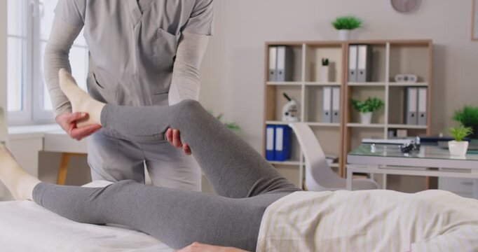 Male physical therapist doing rehabilitation massage for patient in clinic, manual therapy for female knee, posing in medical clinic room. Female trying to reduce disability for body health