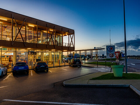 E.Leclerc service station entrance at twilight with illuminated interior signage ("Nos marques sont au m&ecirc;me prix sur autoroute qu'en magasin"), parked cars, and the large "E.Leclerc" pylon sign 
