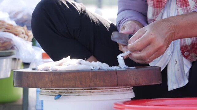 Hands clean and gut small fish on a cutting board outdoors at a market stall. Traditional skills.